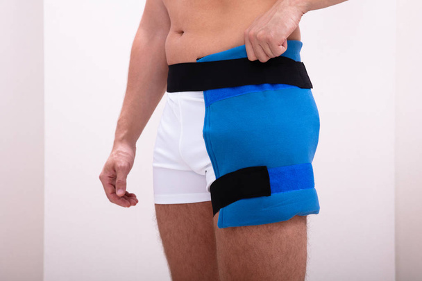 Mid Section Of A Person Wearing Blue Thigh Ice Pack Against White Background - Photo, image