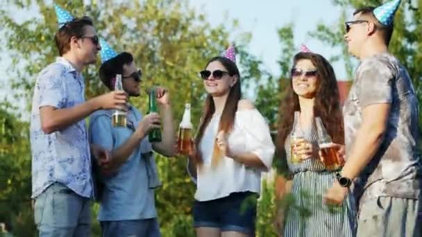 Group of friends drinking beer on nature, young people dancing on summer party, wearing birthday caps - Footage, Video