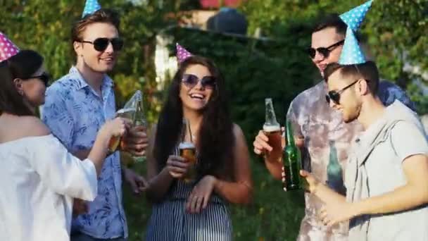 Happy ομάδα φίλων πίνουν μπύρα και χορεύουν σε εξωτερικούς χώρους στο καλοκαιρινό πάρτι, φορώντας καπέλα γενεθλίων - Πλάνα, βίντεο