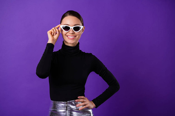 Portrait of charming glad person touching her specs smiling at camera wearing black turtleneck isolated over purple violet background - Fotó, kép