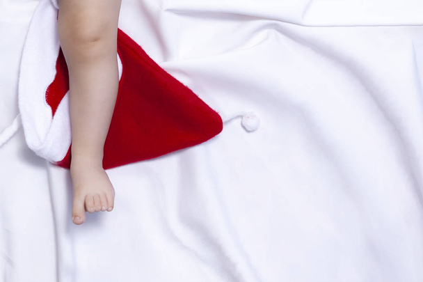 Vista da vicino delle gambe del bambino sul cappello rosso di Babbo Natale. Primo Natale di un neonato
 - Foto, immagini