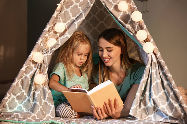 Szczęśliwy kobieta z jej trochę córka czytanie książka w hovel w Dom - Zdjęcie, obraz
