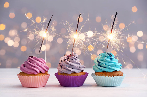 Cupcakes de aniversário saborosos na mesa contra luzes desfocadas
 - Foto, Imagem