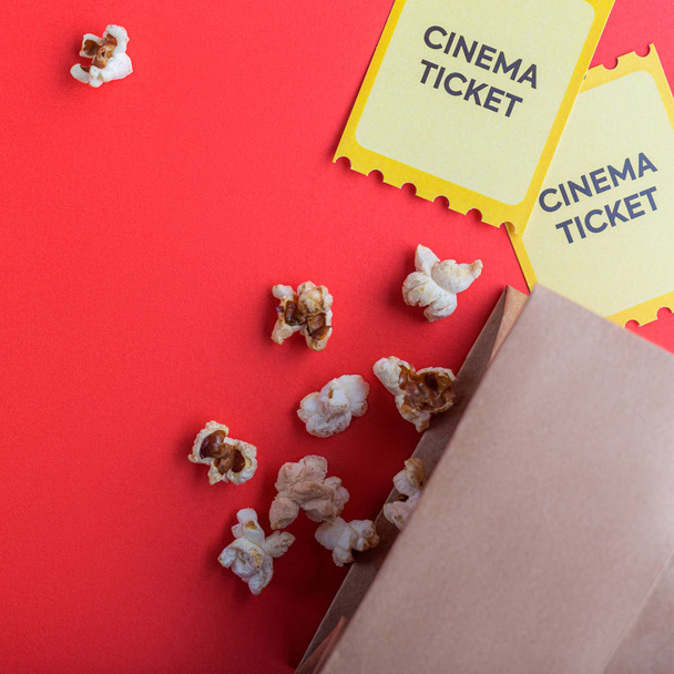 craft bag with popcorn and two yellow cinema tickets on red background flatlay  - Foto, imagen