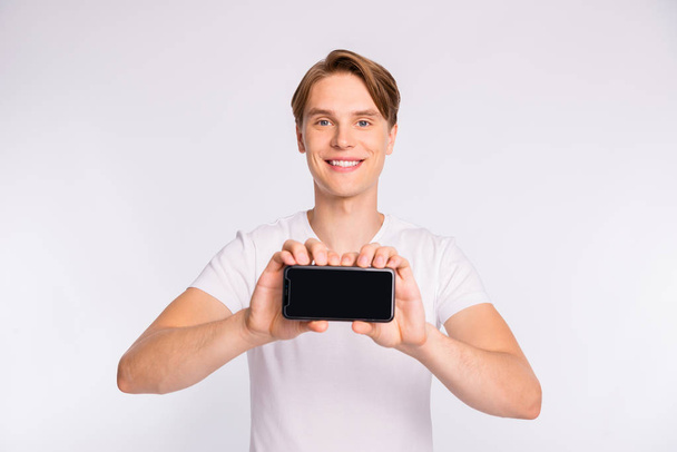 Photo of sales manager guy holding new telephone model wear casual t-shirt isolated white background - Photo, image
