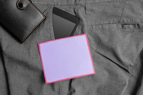 Dispositivo de teléfono inteligente en el bolsillo delantero de los pantalones con una billetera y papel de nota púrpura. Gadget moderno se coloca dentro de los pantalones de hombre cerca de hoja de notación más monedero
 - Foto, imagen