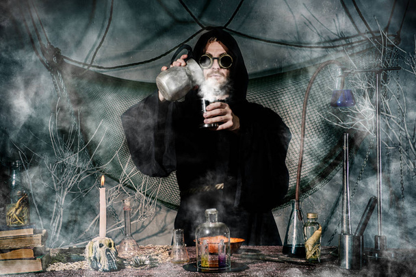 Середньовічний алхімік робить магічний ритуал за столом у своїй димовій лабораторії
. - Фото, зображення