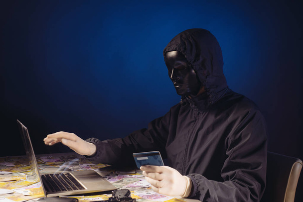 Anonymous hacker in mask programmer uses a laptop to hack the system in the dark. - Photo, Image