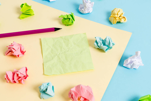 Colored crumpled sheets and a pencil placed around the empty rectangle shaped reminder note in the centre of a blue background and yellow square. Office supplies, fastener. - Photo, image