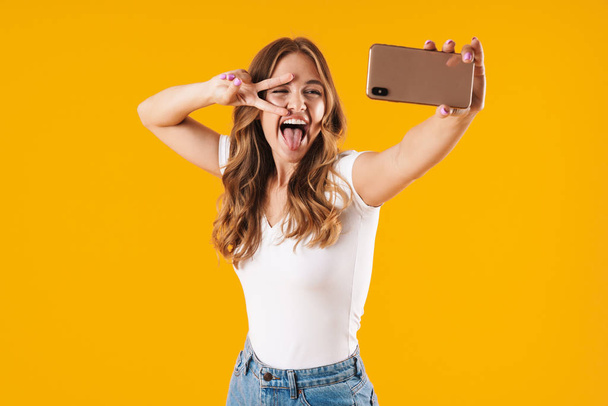Image closeup of excited caucasian woman wearing basic t-shirt showing peace sign while taking selfie photo on cellphone - Фото, зображення