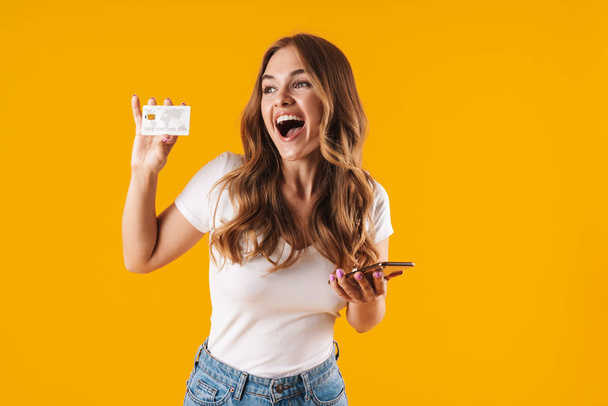 Photo of delighted young woman rejoicing while holding credit card and smartphone - Foto, Bild