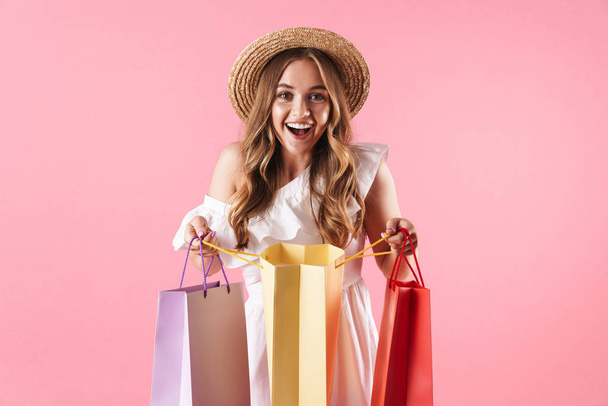 Image of caucasian amazed woman wearing straw hat wondering and holding shopping bags - Foto, imagen