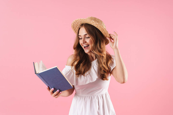 Smiling cute young pretty woman posing isolated over pink wall background reading book. - Foto, imagen