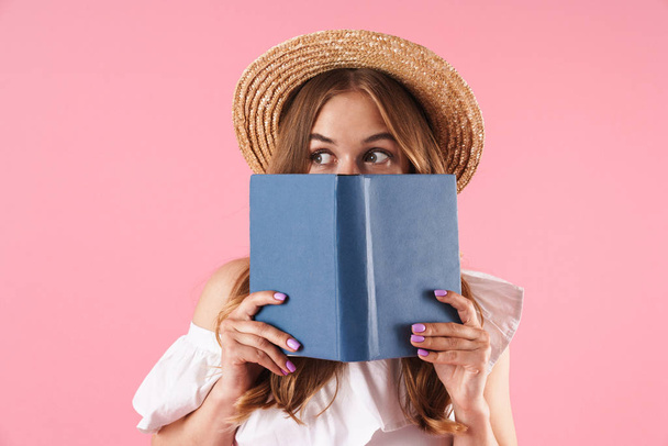 Cute young pretty woman posing isolated over pink wall background with book. - 写真・画像