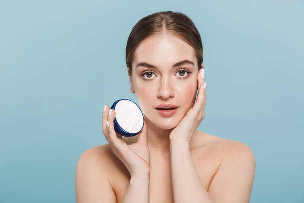Amazing young woman posing isolated over blue wall background take care of her skin with cream. - Φωτογραφία, εικόνα