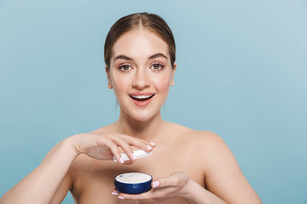 Amazing young woman posing isolated over blue wall background take care of her skin with cream. - Photo, Image