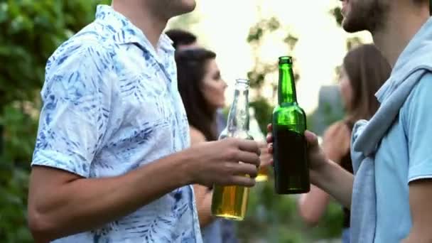 Dos amigos están sosteniendo botellas de cerveza en sus manos y hablando, en el fondo la gente está bailando en la fiesta
 - Imágenes, Vídeo