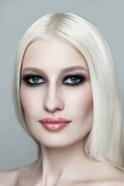 Young blonde woman with smoky eye makeup on grey background - 写真・画像
