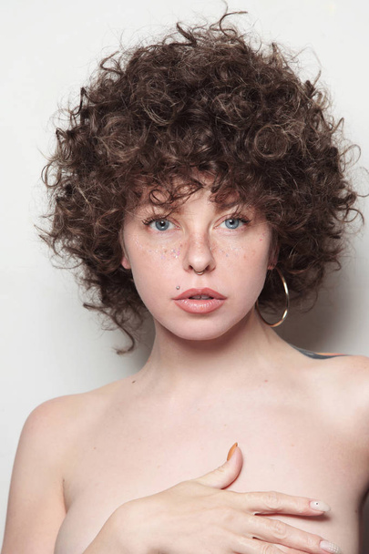 Portrait of young woman with fancy curly hair, glitter freckles and tattoo on white background  - Foto, afbeelding