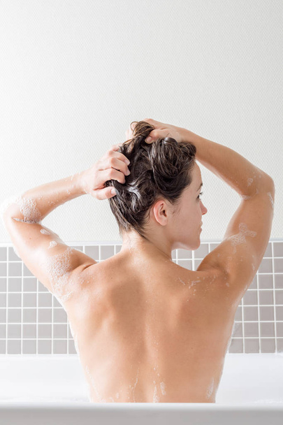 Caucásica chica lavando su cabello dentro de una bañera con espuma
 - Foto, Imagen