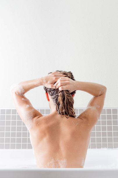 Caucasienne fille laver ses cheveux à l'intérieur d'une baignoire avec de la mousse
 - Photo, image