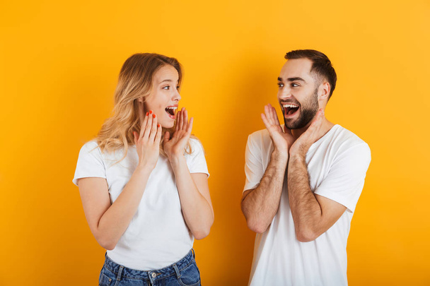 Portrait of optimistic amazed young couple man and woman in basic t-shirts smiling and looking at each other with arms raised - Fotoğraf, Görsel
