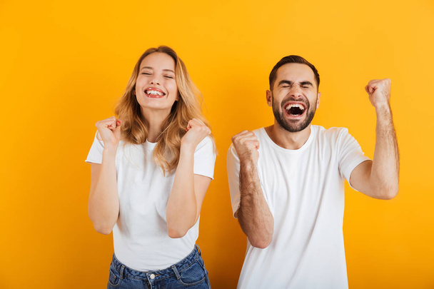 Portrait of joyful astonished couple man and woman in basic t-shirts rejoicing and clenching fists - Foto, imagen