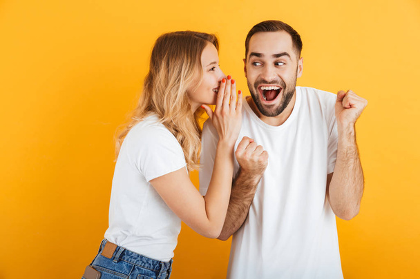 Image of ecstatic couple man and woman in basic t-shirts whispering secrets or gossips to each other - Foto, Imagen