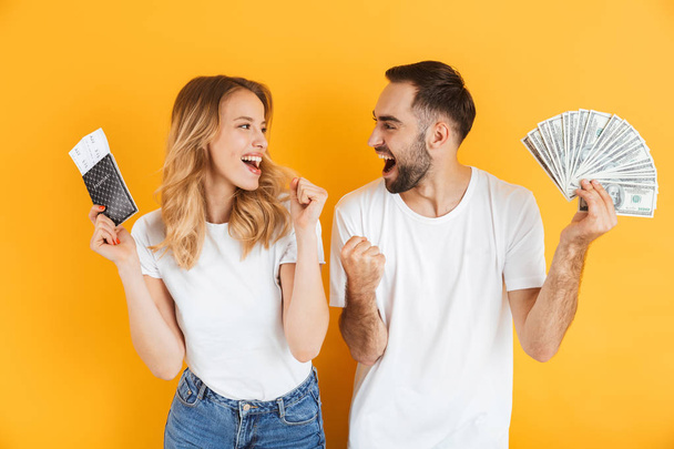 Image of joyous couple rejoicing while holding money cash and passport with travel tickets - Фото, изображение