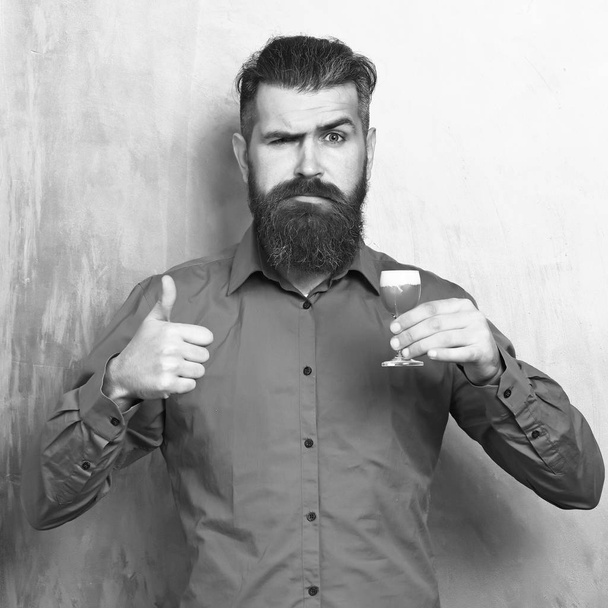 Bearded man, long beard. Brutal caucasian serious hipster with moustache in brown shirt holding alcoholic red shot on golden texture backgroun - Fotoğraf, Görsel