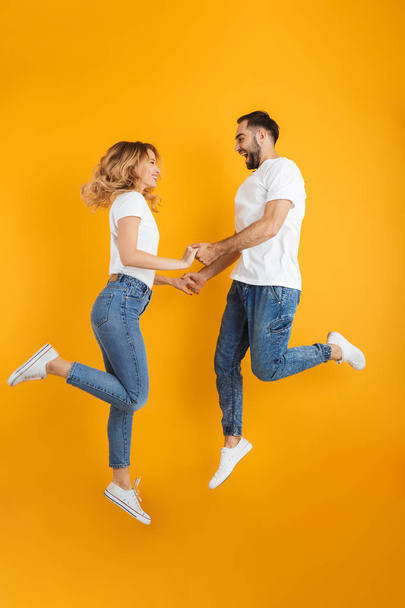 Full length image of joyful couple rejoicing and jumping while holding hands together - Foto, immagini