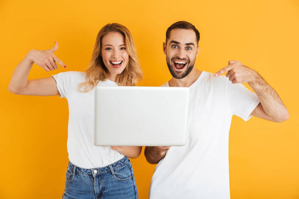 Image of excited couple man and woman rejoicing together while pointing fingers at laptop - 写真・画像