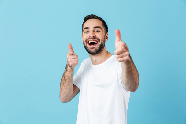Захоплений молодий кричущий щасливий бородатий чоловік позує ізольовано на фоні синьої стіни, вказуючи на вас
. - Фото, зображення