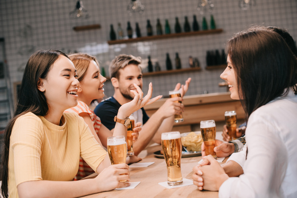 cheerful multicultural friends talking while drinking beer together in pub - Foto, imagen