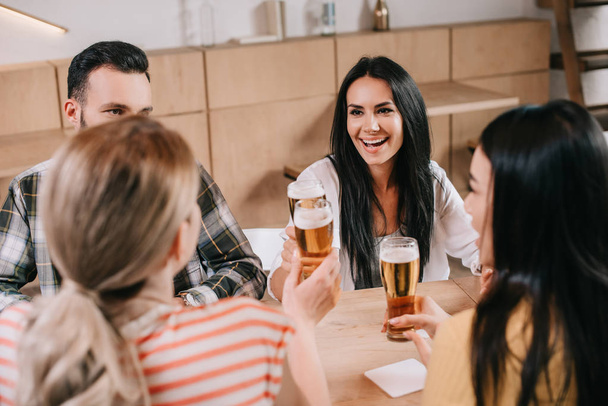 back view of young women clinking glasses of light beer with friends in pub - Foto, imagen