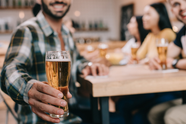 valikoiva painopiste miehen tilalla lasi kevyttä olutta istuessaan pubissa ystävien kanssa
 - Valokuva, kuva