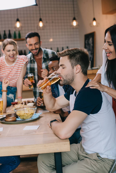 fiatal ember iszik könnyű sör csukott szemmel, míg a kiadási idő pub együtt vidám multikulturális barátok - Fotó, kép