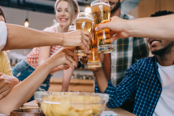 vista parziale di amici multiculturali che tintinnano bicchieri di birra leggera in pub
 - Foto, immagini
