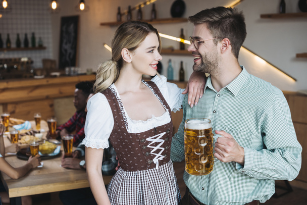attraente cameriera in costume nazionale tedesco in piedi vicino a giovane uomo in possesso di tazza di birra leggera
 - Foto, immagini