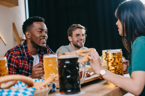 amigos multiculturales alegres sentados cerca de tazas con cerveza clara y oscura en el pub
 - Foto, imagen
