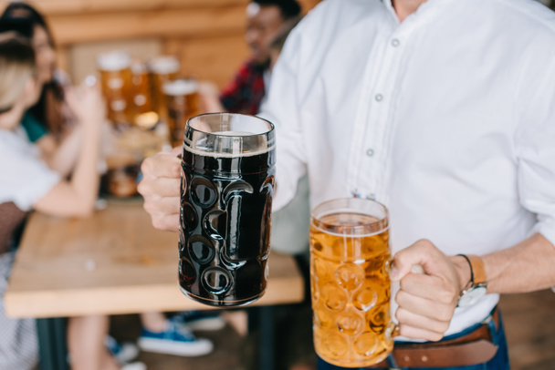 vista ritagliata di giovane uomo che tiene tazze di birra chiara e scura in pub
 - Foto, immagini
