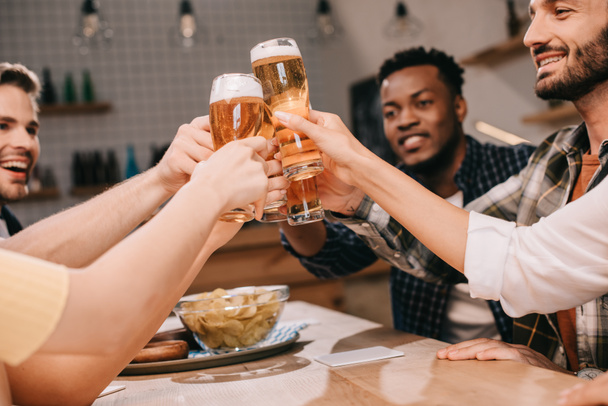 vista parcial de alegres amigos multiculturales tintineo vasos con cerveza lager en el pub
 - Foto, Imagen