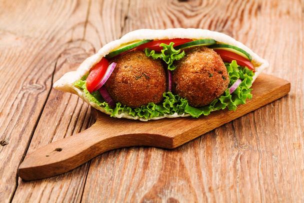 Falafel and fresh vegetables in pita bread on wooden table - 写真・画像