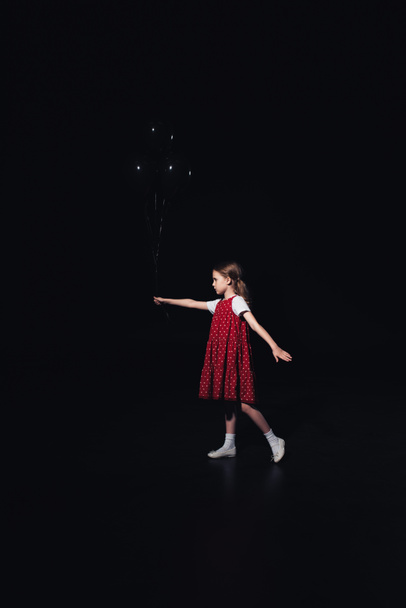 einsames Kind, das mit schwarzen Luftballons auf schwarzem Grund läuft - Foto, Bild