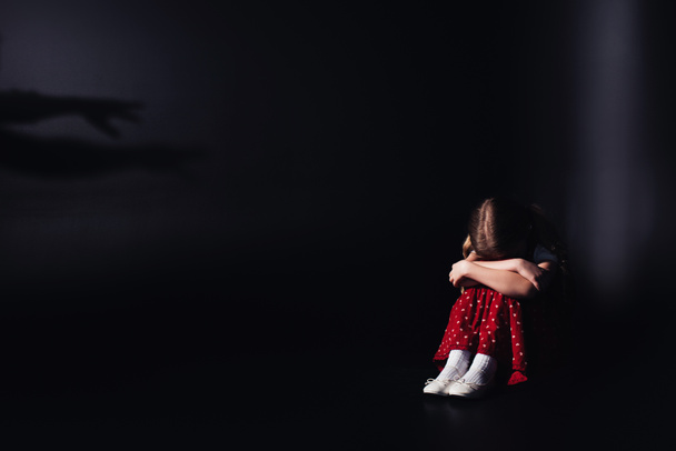 depressives, einsames Kind, das mit gesenktem Kopf auf schwarzem Hintergrund sitzt - Foto, Bild