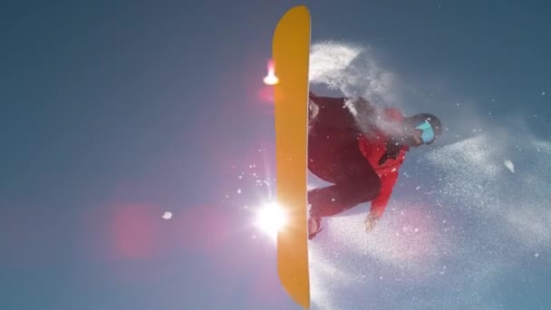 Slow Motion Close Up: Snowboardzista skaczący na dużym kopaczu powietrza, opryskujący płatki śniegu i latający nad słońcem w idealny zimowy dzień. Snowboard skok w snowparku. Promienie słońca świecące obok skaczącego deskorolki w górach - Materiał filmowy, wideo