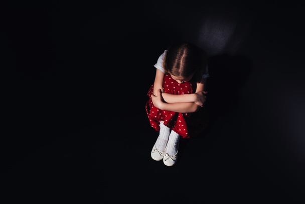 vue aérienne de l'enfant déprimé assis sur le sol sur fond noir
 - Photo, image