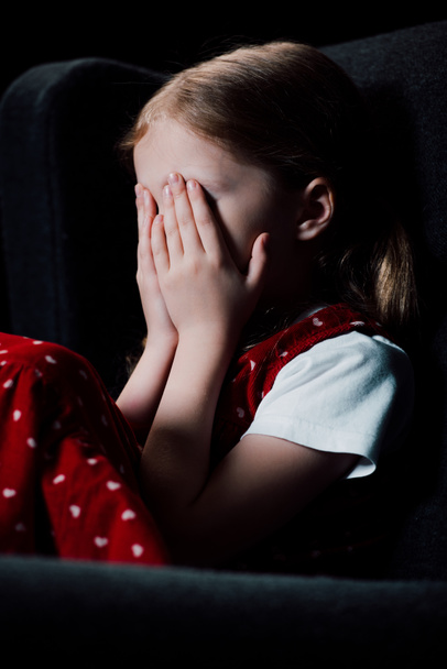 frightened child covering face with hands isolated on black - Photo, Image