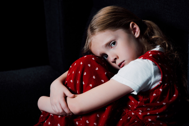 depressed, scared child sitting and looking at camera isolated on black - Foto, Bild