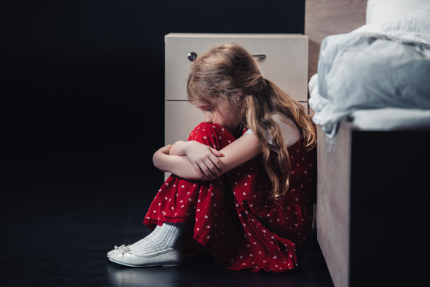 frightened child sitting on floor near bed on black background - Valokuva, kuva